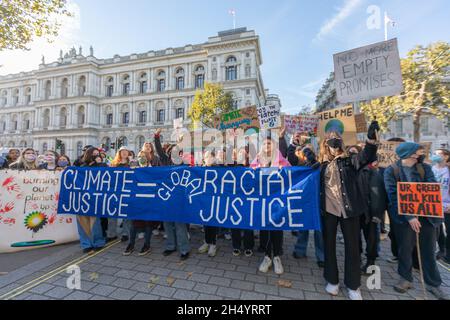 5 novembre 2021. Londres, Royaume-Uni. Une foule nombreuse de manifestants se rassemble devant un grand bâtiment institutionnel lors d’une manifestation climatique qui appelle également à la justice raciale. La bannière centrale indique « JUSTICE CLIMATIQUE » et « JUSTICE RACIALE » avec une illustration du globe, tandis que d’autres pancartes expriment des exigences urgentes telles que « AIDE-MOI », « PLUS DE PROMESSES VIDES » et « NOTRE CUPIDITÉ nous TUERA TOUS ». Les manifestants lèvent les poings et les signes dans une démonstration puissante d'engagement civique, soulignant l'intersection de l'activisme environnemental et de l'équité sociale. Penelope Barritt/Alamy Live News Banque D'Images