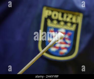 05 novembre 2021, Hessen, Büdingen: Un policier a une baguette d'essai devant le logo de la police hessienne au Wolfgang Konrad Hall dans le district de Lorbach cet après-midi (image symbolique).Un test d'ADN en série aura lieu ici à partir de samedi (06/11/2021) dans la recherche de la mère d'un nourrisson mort trouvé en 1999.Les enquêteurs espèrent que cela les aidera à faire des progrès dans la résolution de l'homicide présumé.Environ 600 femmes de la région entourant la ville dans le district de Wetterau, qui avaient entre 13 et 30 ans quand le corps a été trouvé, ont été invitées à donner volontairement un échantillon de salive.PH Banque D'Images