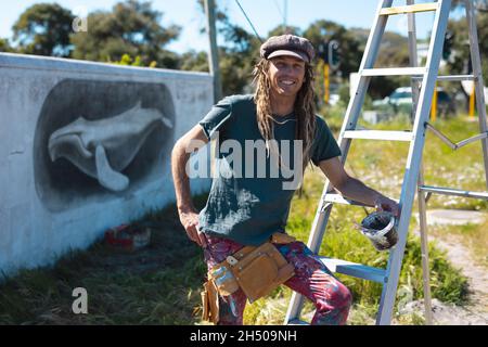 Portrait d'un artiste souriant, appuyé sur une échelle devant la peinture murale de la baleine sur le mur Banque D'Images