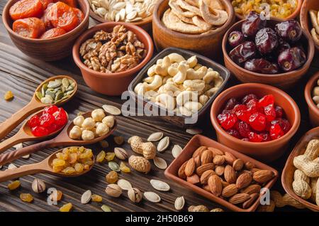 Différentes graines de noix et fruits secs dans des bols et des cuillères sur une table de cuisine en bois Banque D'Images