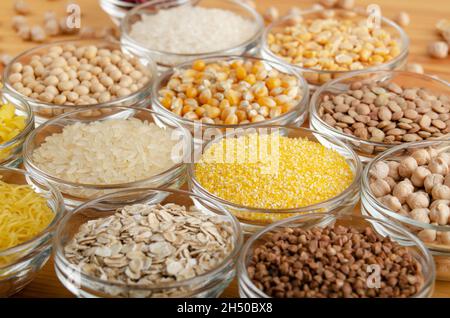 Ensemble de différentes légumineuses et grains dans des bols en verre sur table de cuisine en bois, non périssable, longue durée de conservation concept alimentaire Banque D'Images