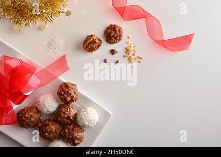 Collation cadeau de Noël avec boules de chocolat avec morceaux d'amande et de noix de coco sur table blanche avec cadeau et décoration de Noël.Vue de dessus. Banque D'Images