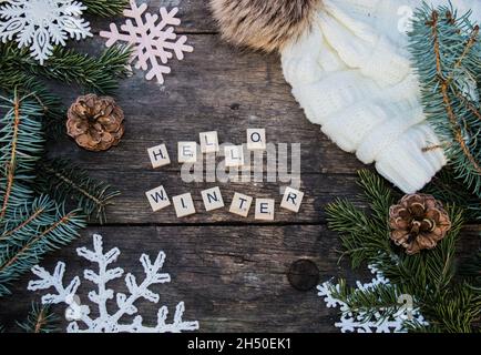décorations en forme de flocon de neige en crochet sur sol en bois avec textes d'hiver et branches et cônes en sapin et fond de chapeau de galet tricoté Banque D'Images