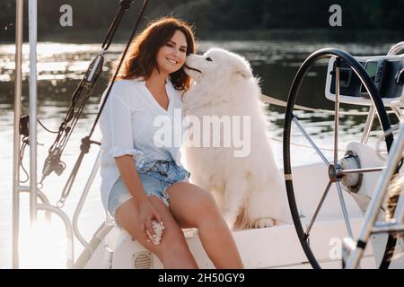 Une femme heureuse avec un grand chien blanc sur un yacht blanc à la mer.le chien chuchote dans mon oreille. Banque D'Images