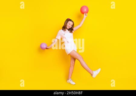 Vue sur toute la longueur du corps de la jolie fille gaie tenant des boules d'air dansant havin amusant temps libre isolé sur fond jaune vif de couleur Banque D'Images