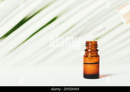 L'huile essentielle s'écoule de la pipette à la bouteille sur fond blanc avec une feuille verte.Copier l'espace Banque D'Images