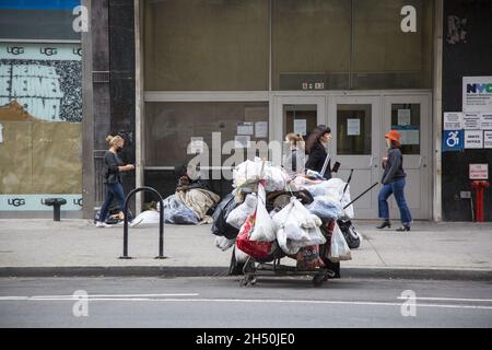 Les sacs d'affaires pour hommes sans-abri sont garés sur la 14e rue en face de Union Square pendant qu'il dort sur le trottoir au milieu des passants de Manhattan, New York. Banque D'Images