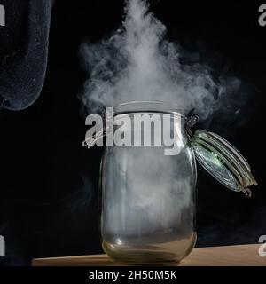 Pot en verre avec couvercle rempli de fumée sur fond noir.Brouillard dans un récipient transparent sur la table. Banque D'Images