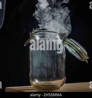 Pot en verre avec couvercle rempli de fumée sur fond noir.Brouillard dans un récipient transparent sur la table. Banque D'Images