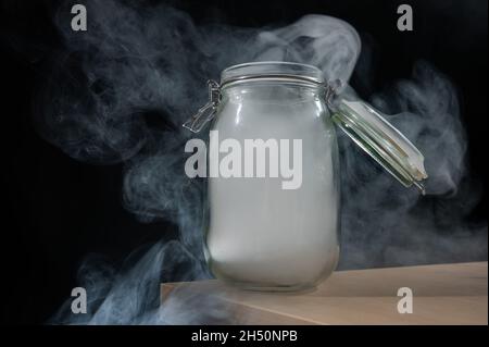 Pot en verre avec couvercle rempli de fumée sur fond noir.Brouillard dans un récipient transparent sur la table. Banque D'Images