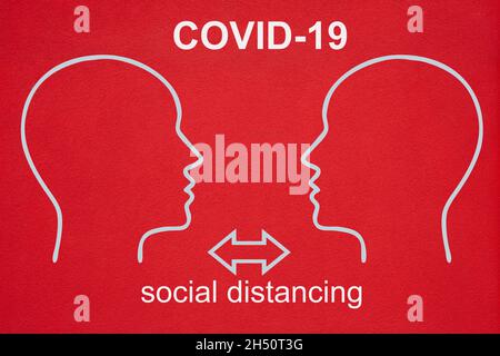 Deux contours de têtes en blanc se font face l'un à l'autre.Le texte CORVID-19 et la distanciation sociale est écrit sur le fond rouge de la cheminée.Deux flèches pointent Banque D'Images