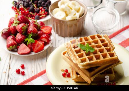 Pile de trois gaufres belges sur une table de cuisine blanche avec fraises, bananes et cassis Banque D'Images