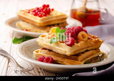 Gaufres belges servies avec framboises et feuilles de menthe sur blanc table de cuisine en bois avec sirop de côté Banque D'Images