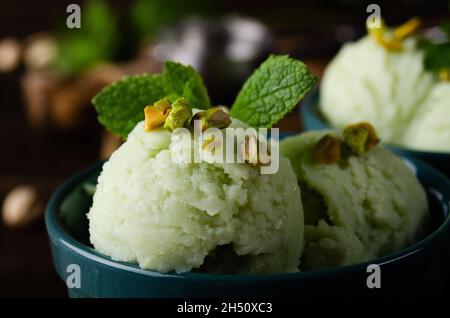 Boules de glace de pistache dans des bols en argile sur une table de cuisine en bois avec chapelure et noix de côté Banque D'Images