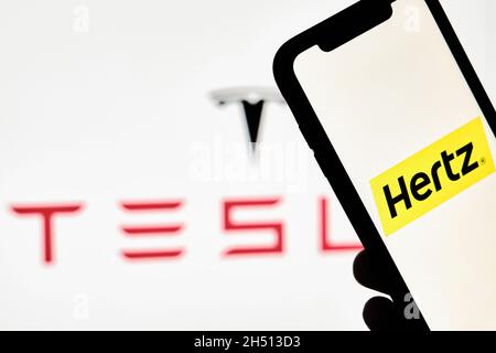 Tashkent, Ouzbékistan - 29 octobre 2021 : une personne porte un smartphone avec la marque Hertz sur fond de logo Tesla.Commande Hertz pour Tesla Electric Banque D'Images