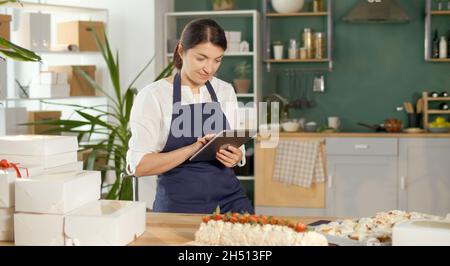 Une femme d'affaires prospère gérant ses travaux d'affaires dans une cuisine confortable Banque D'Images