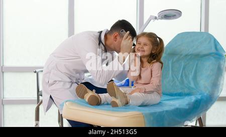 Un médecin traitant examine l'oreille d'une petite fille à l'aide d'un dispositif spécial. Banque D'Images