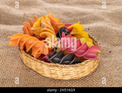 Pâtes fusilli de couleur crue dans un plat de paille sur le talus, gros plan. Banque D'Images