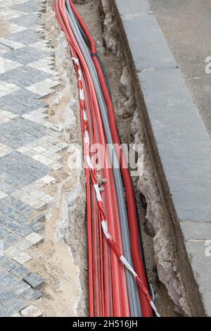Un grand nombre de câbles de réseau Internet électriques et à haute vitesse dans un tuyau ondulé rouge sont enterrés sous terre dans la rue couverte de pavés Banque D'Images