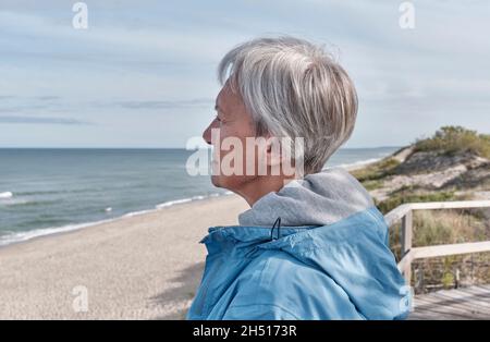 Femme sénior sérieuse avec de courts cheveux gris sur le bord de la mer regardant dans la distance.Gros plan Banque D'Images