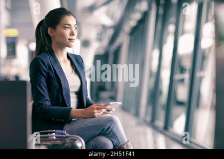 Téléphone portable Voyage femme d'affaires attendant dans le salon de l'aéroport avec des bagages à main.Jeune femme asiatique en voyage d'affaires avec un téléphone portable.Appareil de technologie Banque D'Images