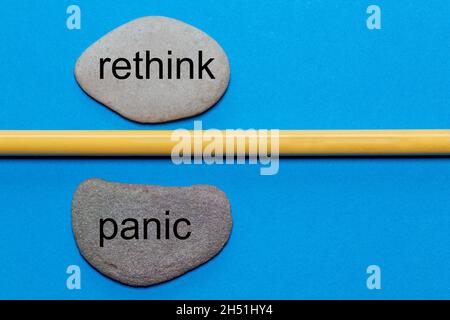 Les mots Reethink et Panic sont écrits sur des pierres naturelles lisses séparées par un crayon jaune.Le fond est isolé en bleu et a beaucoup de spa Banque D'Images