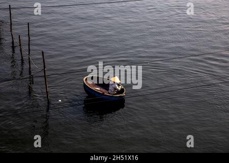 Une personne avec chapeau conique flottant dans un panier rond sur la rivière Trường Giang. Banque D'Images