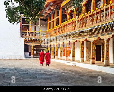 Deux moines bouddhistes dans leur robe rouge traditionnelle marchant dans la cour du monastère Punakha Dzong, Bhoutan. Banque D'Images