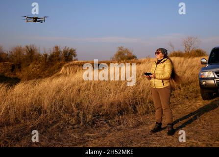 Belle femme pilote drone sur voiture tout-terrain et automne herbe fond. Banque D'Images