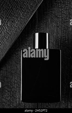 Il s'agit d'une photo promotionnelle de l'eau de toilette ou du parfum dans un style sombre.Bouteille noire sur le fond d'un arbre brûlé.Mise en page pour le logo ou les informations de vente ou le Vendredi fou. Banque D'Images