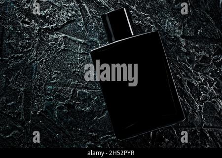 Parfum ou eau de toilette pour hommes.Photo promotionnelle d'une bouteille noire sur fond sombre.Mise en page pour la copie de texte. Banque D'Images