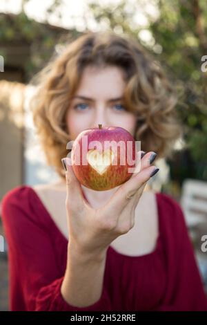 belle jeune femme tient une pomme rouge avec un coeur sculpté en face de son visage. attention sélective à la pomme.Bonne nutrition en vitamines.Surp Banque D'Images