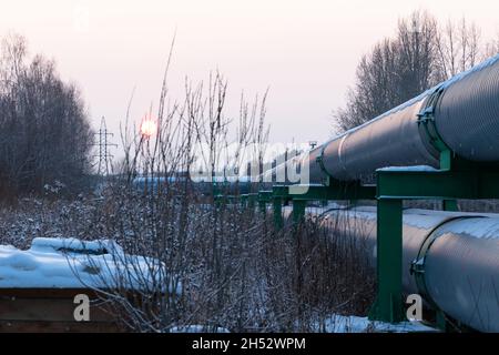tuyaux de chauffage central dans une gaine d'isolation thermique métallique de protection posé au-dessus du sol lors d'une soirée d'hiver froide à coucher de soleil Banque D'Images