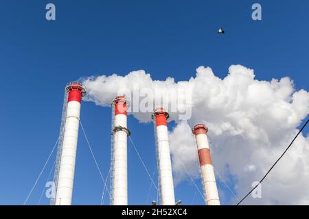 cheminées rouge-blanc de la chaufferie, équipées d'un feu de circulation. fumée blanche contre le ciel bleu le jour d'hiver ensoleillé gelé Banque D'Images