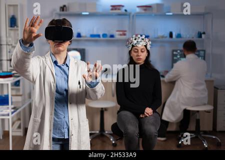 Neurologue médecin spécialiste avec casque de réalité virtuelle analysant l'évolution du cerveau au cours d'une expérience en neuroscience en laboratoire médical.Femme avec un scanner eeg présentant une maladie neurologique Banque D'Images