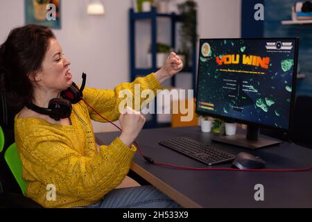 Excitée heureuse gagnante de la compétition femme gamer gagnant jeux vidéo de tir spatial pendant le championnat en ligne célébrant le jeu à la maison dans le salon.Lecteur jouant sur un ordinateur puissant RVB Banque D'Images