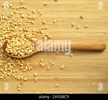 Beaucoup de grain de blé sec dans une cuillère en bois, sur la planche à découper en bambou Banque D'Images