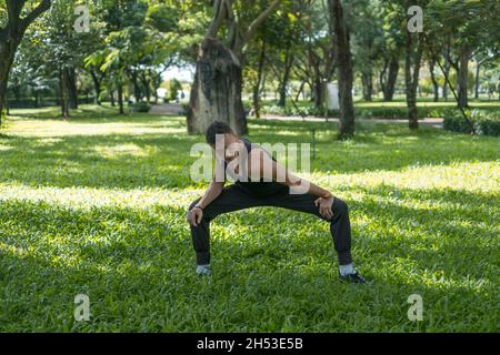 Sportif actif jeune homme en noir sportswear faire des exercices de sport dans le parc.Portrait d'homme de forme beau faisant de l'exercice d'étirement à l'extérieur. Banque D'Images