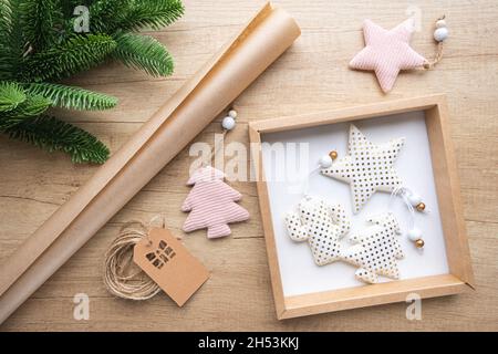 Boîte cadeau avec jouets de Noël en tissu blanc à pois d'or, rouleau de papier kraft, branche de sapin sur fond de bois.Concept d'emballage écologique, zéro Banque D'Images