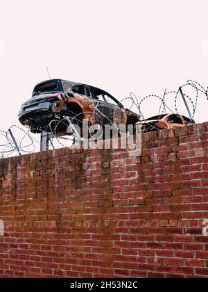 Un grattoir de métal avec des carrosseries de voiture endommagées derrière un mur avec des fils barbelés - cour de disjoncteurs de voiture en métal - recyclage de voiture Banque D'Images