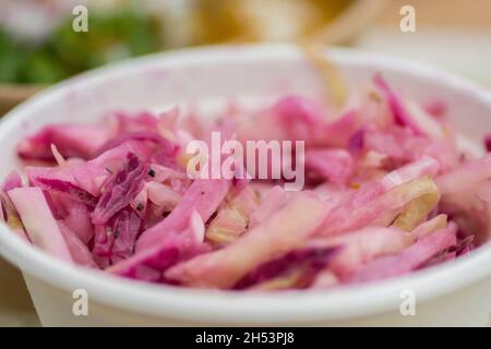 Salade rose de chou frais et d'oignons rouges, servie dans un bol en papier blanc Banque D'Images