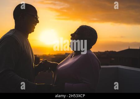 Couple latin senior heureux ayant un moment romantique dansant sur le toit au coucher du soleil Banque D'Images