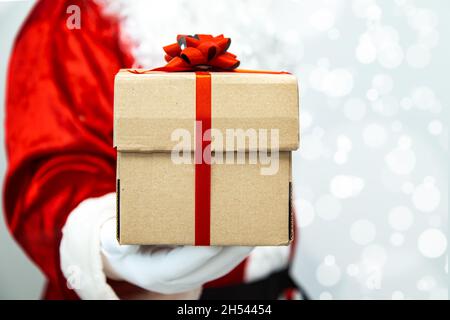 Le Père noël a des mains gantées tenant une boîte cadeau avec un ruban rouge. Banque D'Images