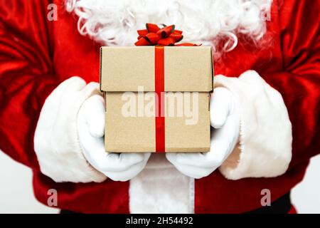 Le Père noël a des mains gantées tenant une boîte cadeau avec un ruban rouge. Banque D'Images