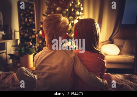 Les enfants s'assoient dans le lit et regardent l'arbre de Noël.Décorations de Noël, en attente des vacances. Banque D'Images