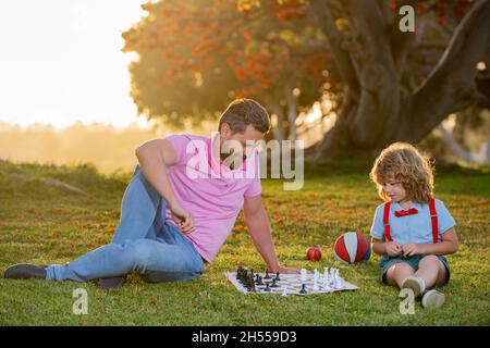 Le père joue aux échecs avec son fils.École d'échecs pour enfants.Famille en extérieur. Banque D'Images