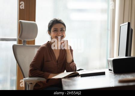 Femme d'affaires indienne souriante assise sur un bureau pour un appareil photo Banque D'Images