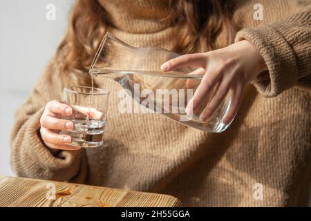 Une femme verse de l'eau dans un verre à partir d'une carafe en verre. Banque D'Images