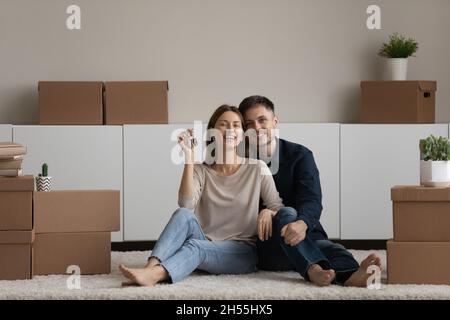 Portrait couple heureux démontrant les clés, assis sur le sol, appréciant la réinstallation Banque D'Images