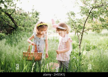 Chasse aux œufs de Pâques. Groupe d'enfants portant des oreilles de lapin courant pour ramasser des œufs colorés lors de la chasse aux œufs de Pâques dans le jardin. Tradition de Pâques Banque D'Images